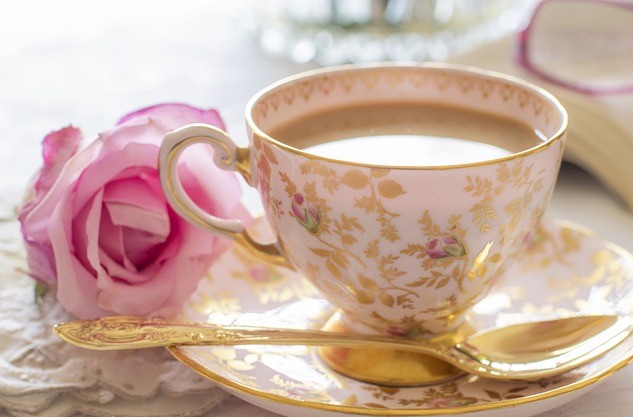A china cup of tea with a pink rose next to it to illustrate love and care