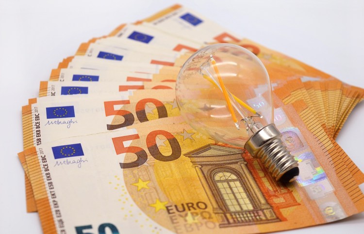 A lightbulb on a pile of 50 euro notes to illustrate with great power comes an even greater electricity bill
