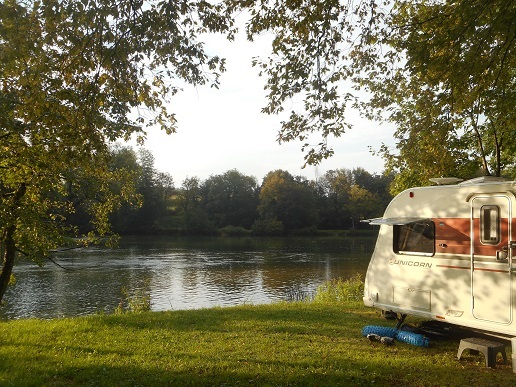 Caravan parked by tranquil river amid greenery