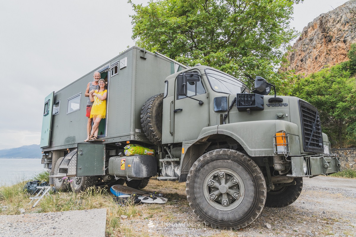 A picture of The Beast, a 6x4-wheel drive Volvo N10 ex-army truck converted into a camper with author Jacqueline Lambert standing in its doorway in a yellow dress