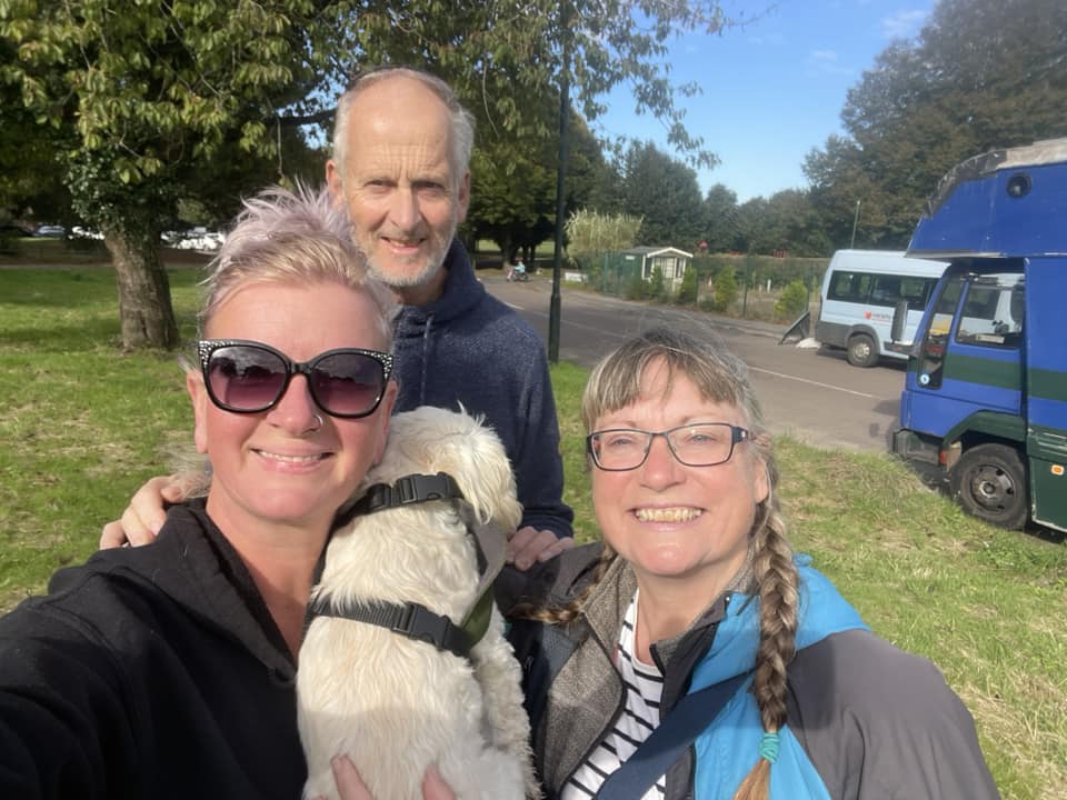 A selfie featuring Nicole and her small white dog Sandy, with me and my husband Mark in the sunshine on the day she set out for Morocco with her blue converted horsebox in the background