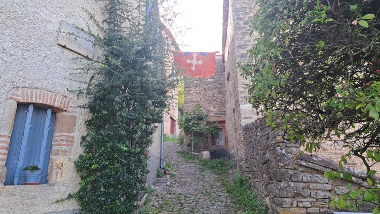 A narrow cobbled street ascending into Cordes-sur-Ciel with an Occitan Cross flag strung across