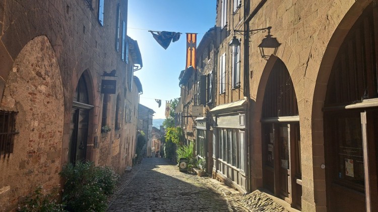Sunlit street in Cordes-sur-Ciel, with flags strung across and Gothic Arches