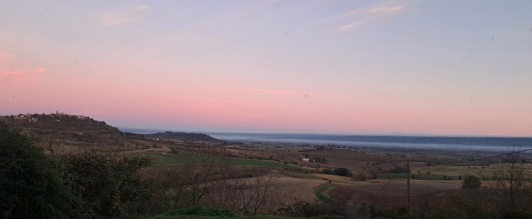 Photo of a misty morning over the medieval hill town of Fanjeaux, with a pink sky and a cloud inversion in the valley in front of the Black Mountains in the distance